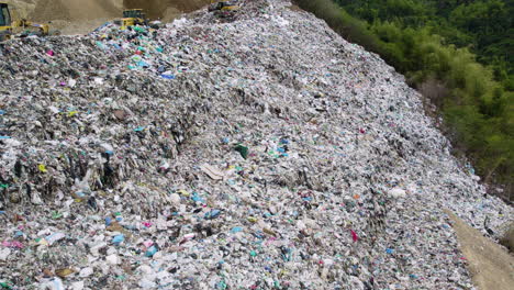 Drone-shot-of-a-landfill-with-trucks-and-tractors-managing-garbage,-highlighting-waste-disposal-and-recycling-efforts