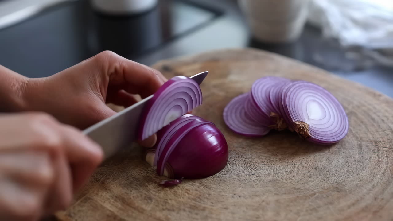 Hands slicing a red onion on a wooden cutting board