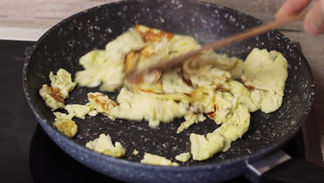 huevos revueltos secos en una sartén negra revueltos con una espátula de madera, de cerca
