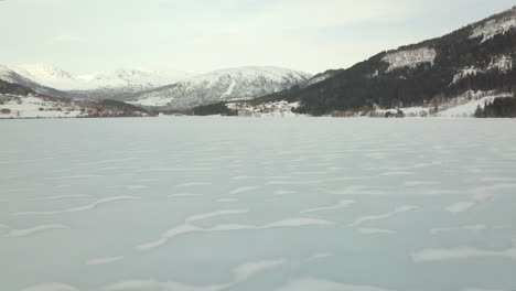 Aerial-View-of-a-Barren,-Frozen-Lake-in-Norway-with-Small-Waves-of-Snow-on-the-Surface,-Forward-Drone-Motion