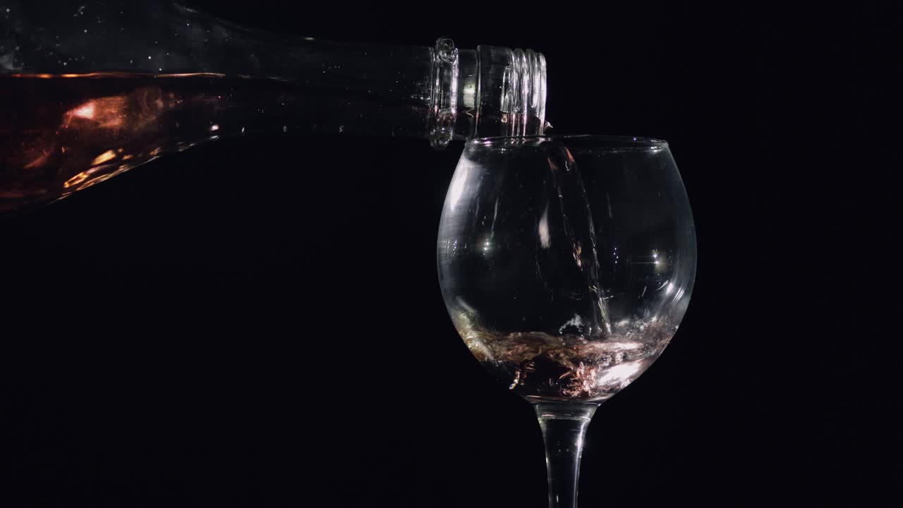 Pouring pink champagne from bottle into glass. Black background