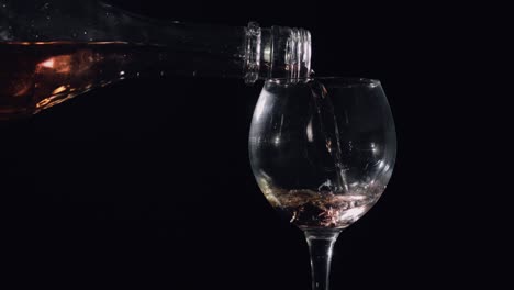 pouring pink champagne from bottle into glass. black background