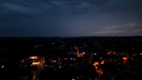 aerial view of small american town at night, glowing warmly under a dark blue sky. streetlights and buildings create peaceful atmosphere. drone wide shot. dusk scene with lighting lantern in city