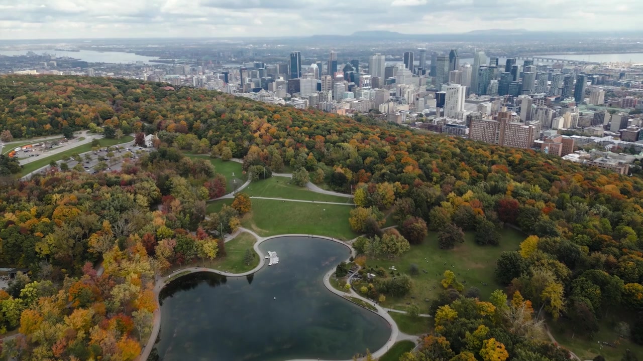 Herbstliche Drohnenansicht des Mount Royal Parks mit dem Bibersee, farbenfrohem Herbstlaub und der Skyline der Innenstadt von Montreal in Kanada.