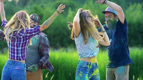 dos parejas jóvenes multiétnicas bailando alegremente y celebrando el festival holi con pinturas en el campo verde