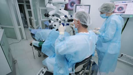 ophthalmological surgery specialist sits in front of microscope performing operation. low angle view on the female doctor conducting high-precision surgery. femto laser assisted cataract surgery.