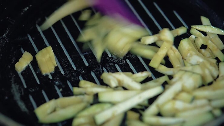 Slices of eggplant are fried in a frying pan in oil the cook mixes them with a spatula