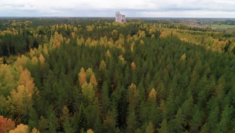 aerial, drone shot, over a colorful trees and towards an old factory building, on the countryside, on a cloudy, day, in uusimaa, finland