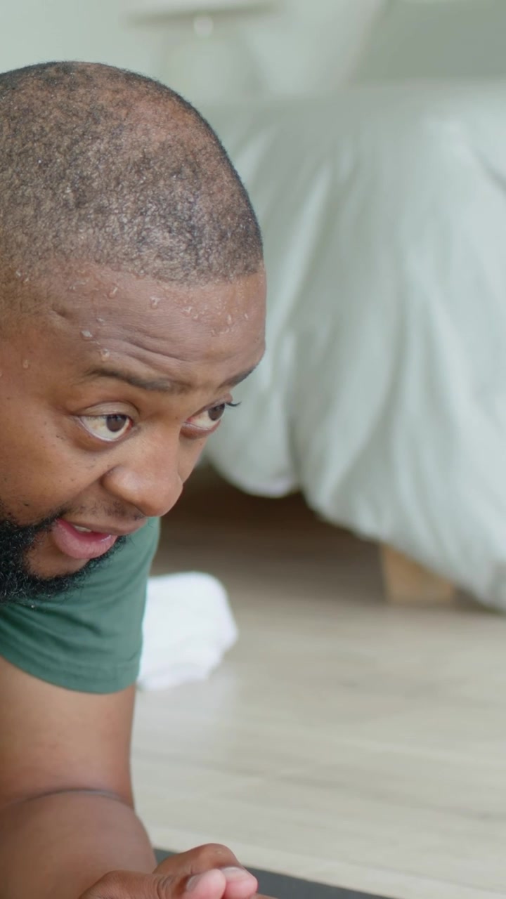 Vertical video: Planking man wearing green tee on bedroom mat, noticing offscreen timer, towel