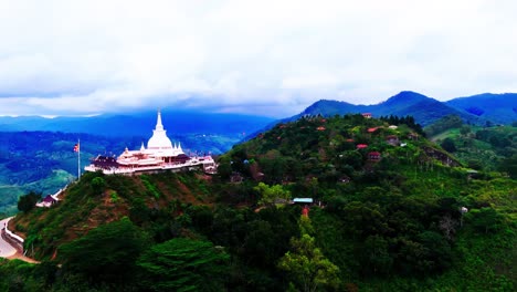 a prominent sri lankan hilltop stupa and temple set against a backdrop of green mountains, scattered hillside houses, tropical vegetation, and sweeping landscape views.