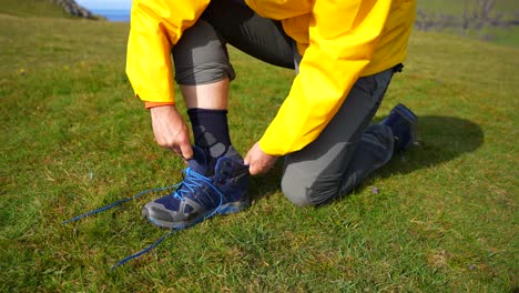 primer plano de un excursionista masculino arrodillado y limpiando su calcetín para ponerse una bota
