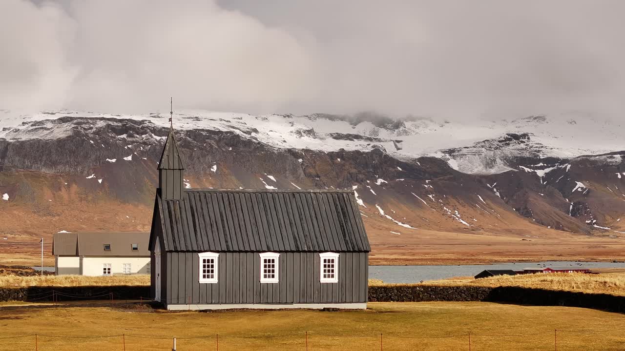 Búðakirkja, Iceland's iconic black wooden church, stands against a dramatic Snæfellsnes backdrop of lava fields and golden sands, reflecting its historical charm and unique isolation.