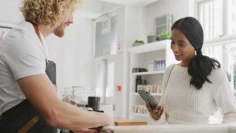 barista masculino y cliente femenino felices pagando con su teléfono inteligente en el café.