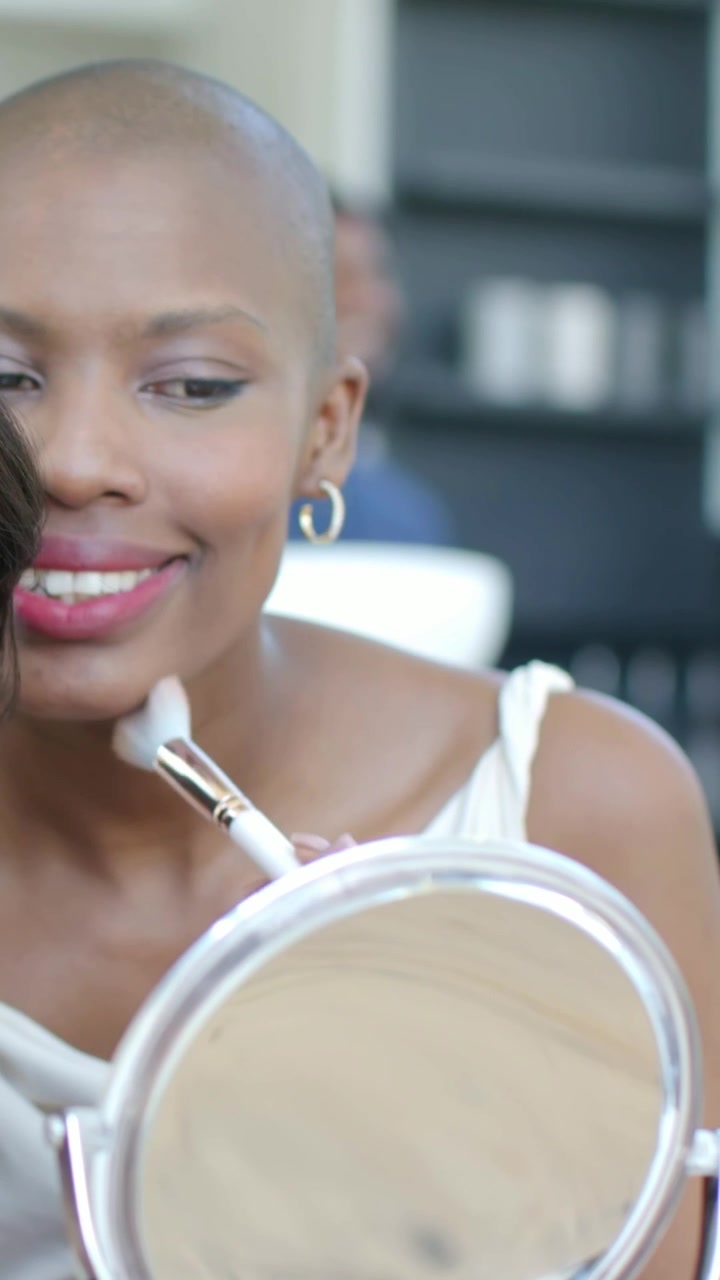 Vertical video: Raising mirror, woman blending makeup at vanity, preparing with brush, white top
