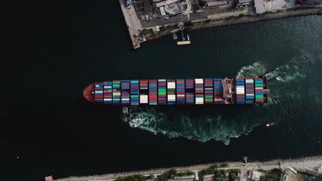 mega large ulcv container ship fully loaded with crates, sailing away from the harbor - birds eye, aerial view