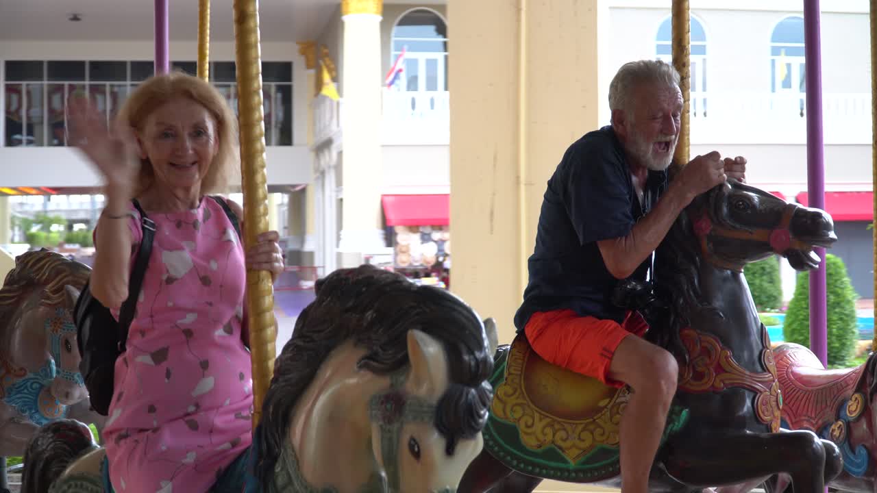 una pareja de ancianos felices montando juntos en un carrusel en el parque de atracciones al aire libre en verano. un anciano loco y una mujer madura divertida divirtiéndose en vacaciones.