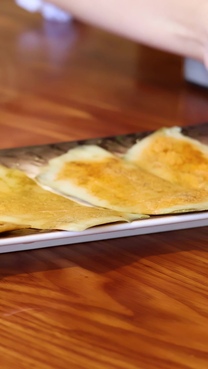 A person places a platter of golden Vietnamese crepes on a rustic wooden restaurant table.