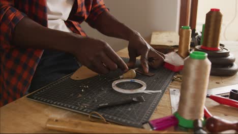 Close up of hands of african american craftsman using tools in leather workshop