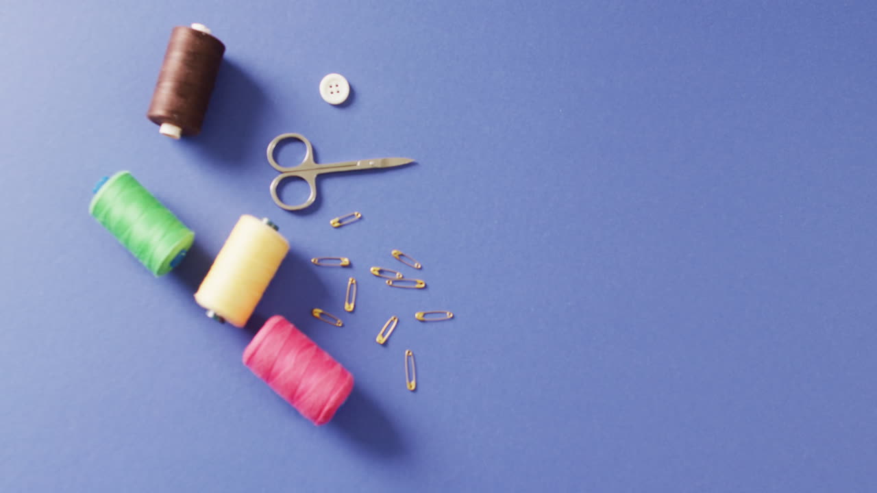 Video of scissors, safety pins, a button and reels of thread on blue background with copy space