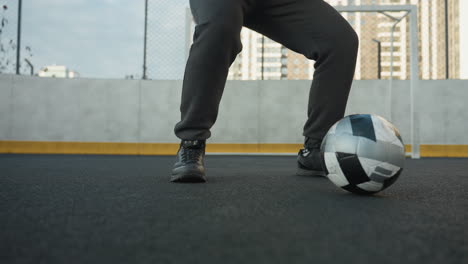 lower angle view of man in squatting position with hands clasped, performing intense workout on outdoor sports ground with soccer ball rolling on ground and urban building in background