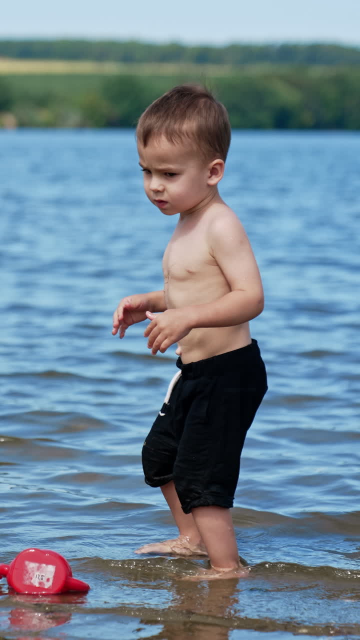 Cute toddler enjoying water in the river. Kid takes some water and touching his belly. Vertical video