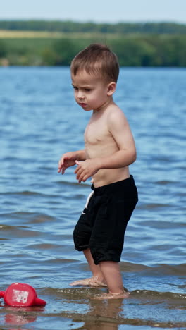 cute toddler enjoying water in the river. kid takes some water and touching his belly. vertical video