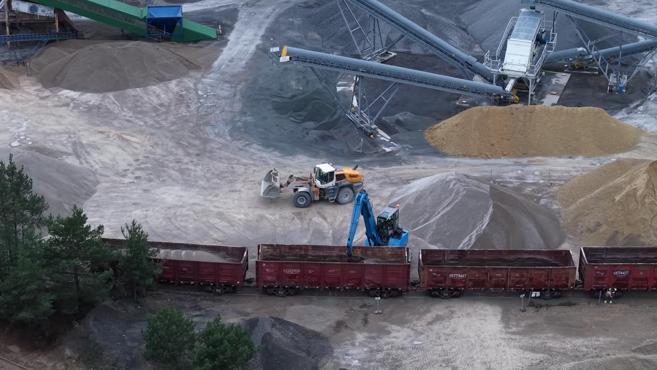 Heavy machinery loading train wagons, aerial drone view