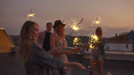 Young-six-people-on-the-roof-move-and-dance-on-a-summer-evening-with-big-bengal-light.-It's-a-pleasure-sunset-before-night.