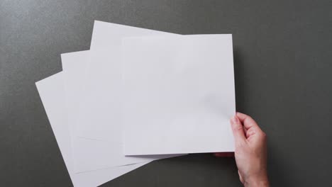 Hand-holding-piece-of-paper-over-pieces-of-paper-with-copy-space-on-gray-background-in-slow-motion