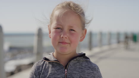 close up portrait of cute little blonde girl looking pensive serious at camera carefree child seaside beach