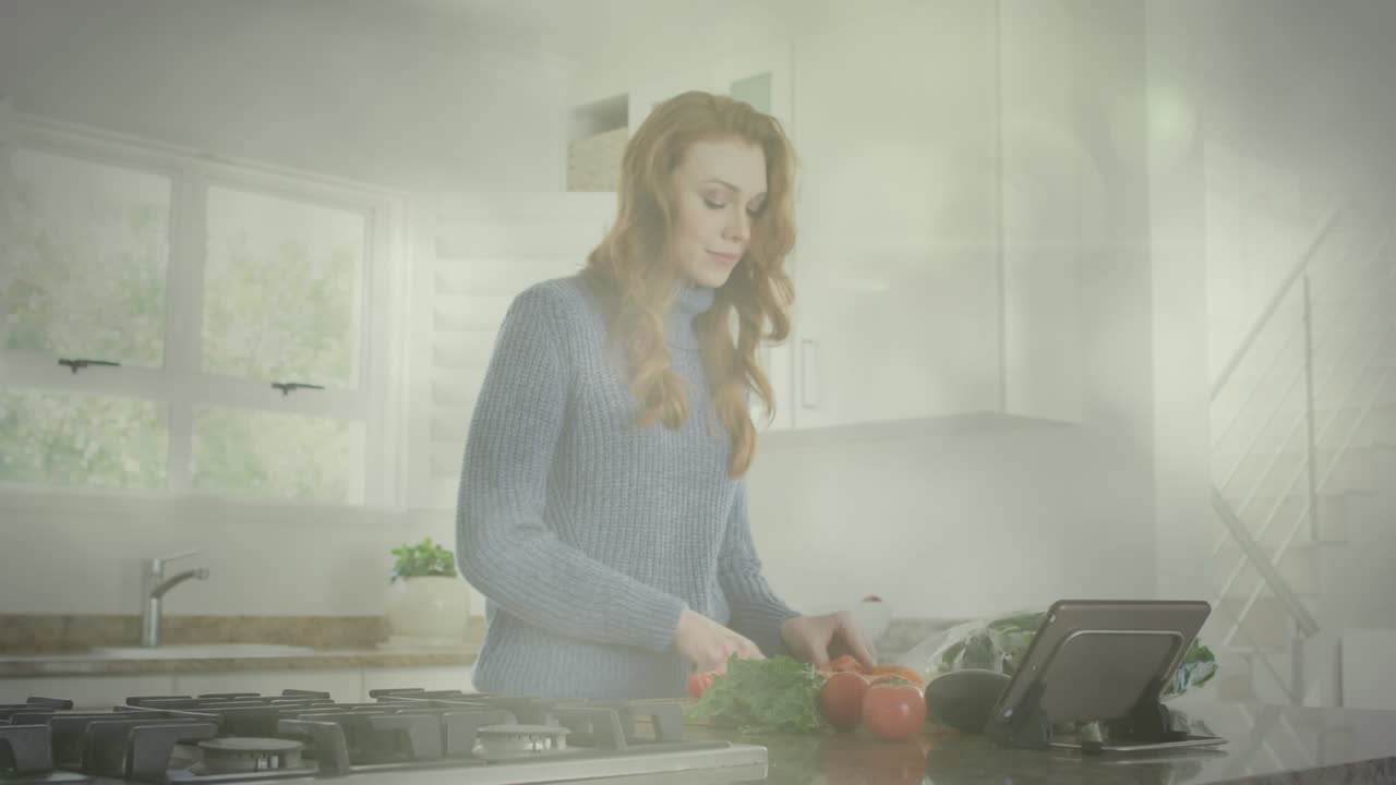 Animazione di punti luce su donna caucasica che taglia le verdure e usa il tablet in cucina.