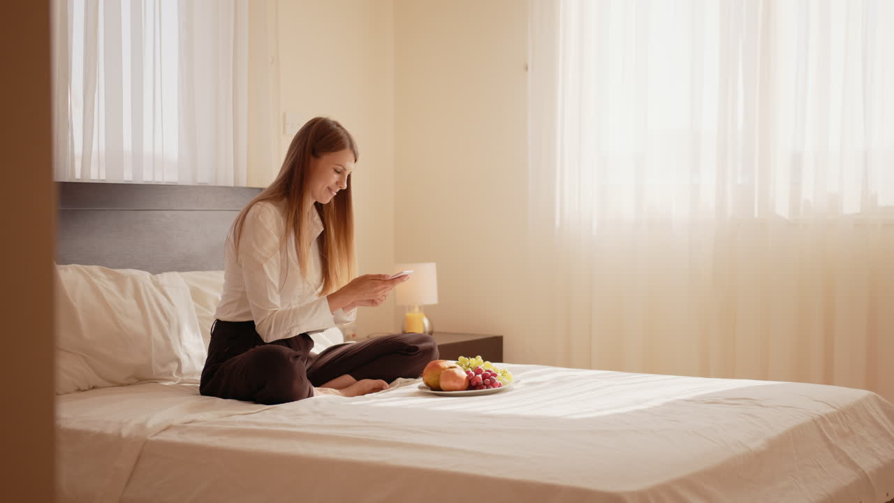 여자 는 전화 와 과일 을 가지고 침대 에서 휴식을 취하고 있다