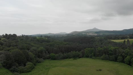 Top-view-shot-of-Irish-mountains-in-the-background-flying-oer-a-green-field