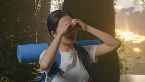 close up of asian female hiker with mountaineering backpack making binoculars gesture looking at something then saying wow while exploring forest nature