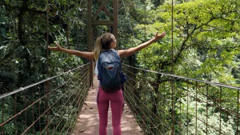 mujer joven caminando en un puente colgante caminando en la selva tropical de costa rica disfrutando de la naturaleza y el parque nacional. aventura de viaje en solitario