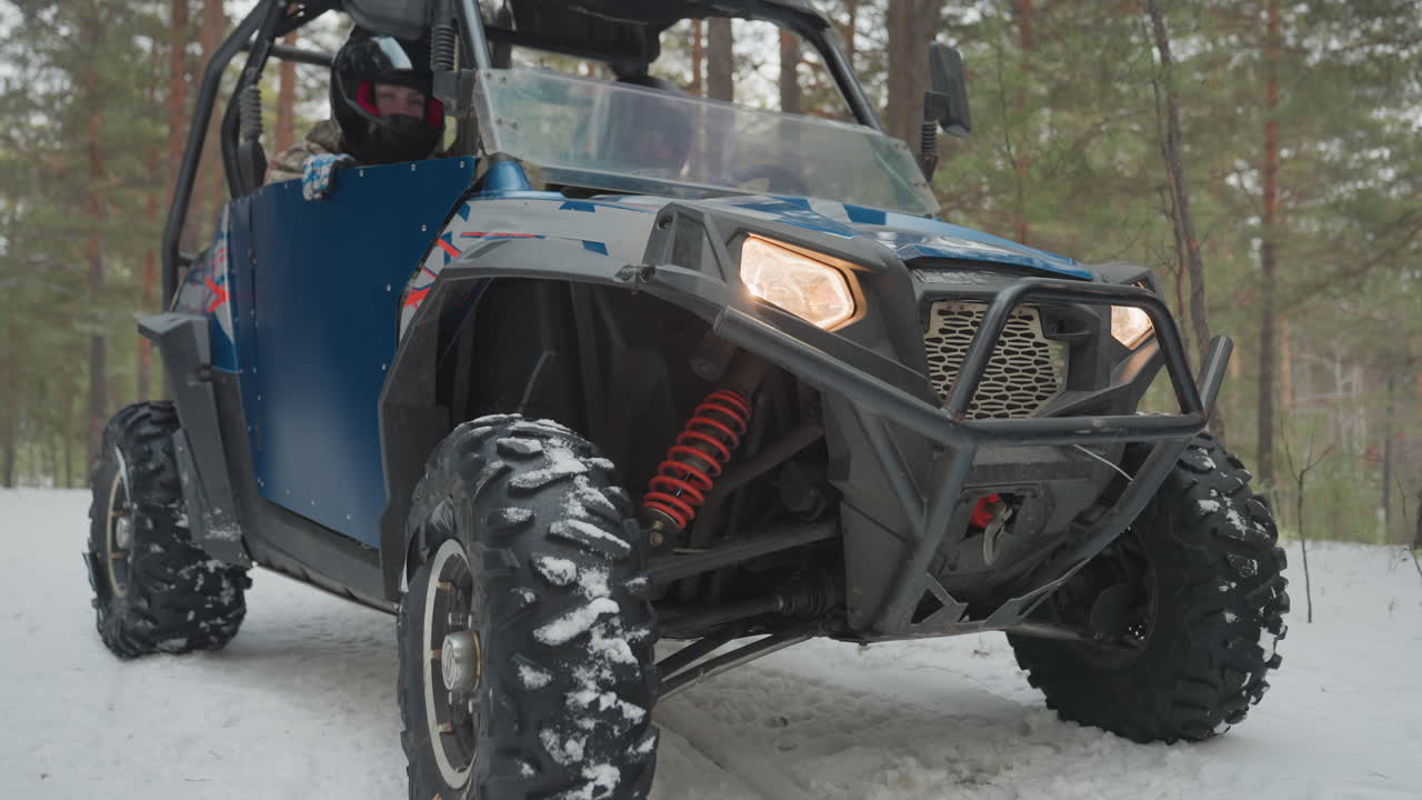Valutazione del quad nella foresta innevata. Veicolo fuoristrada esaminato in un ambiente forestale innevato per la sicurezza. Il pilota controlla attentamente il quad per assicurarsi che funzioni correttamente in condizioni invernali innevate.