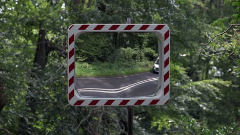 a convex road safety mirror set in woodland at a road junction as vehicles pass by, worcestershire, england