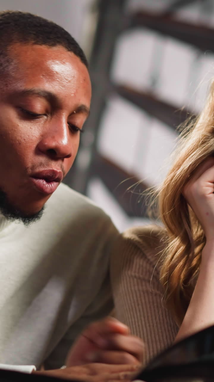 African-American bearded man with beloved white blonde woman looks at pictures of relatives in photobook in living room closeup slow motion