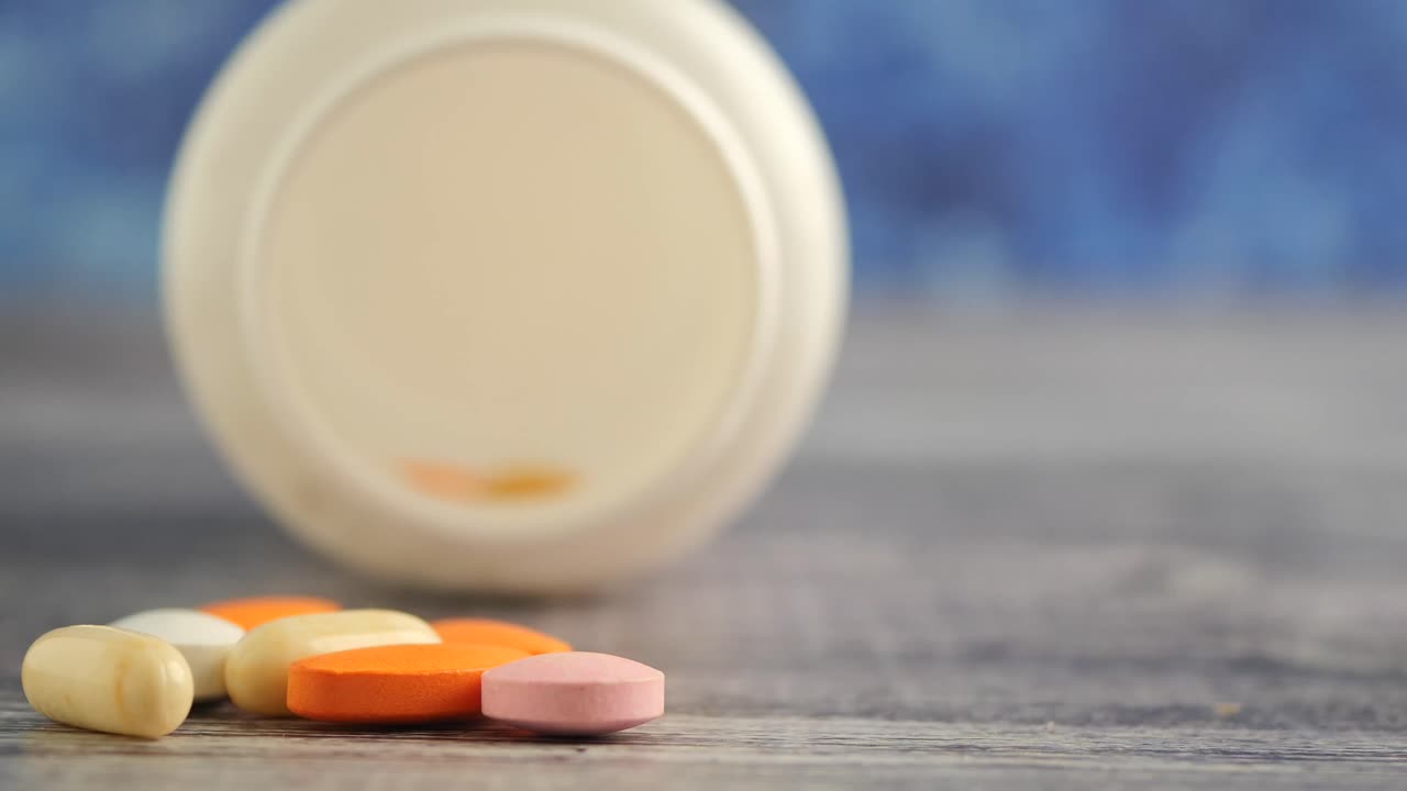Colorful pills spilled from a bottle on a wooden surface