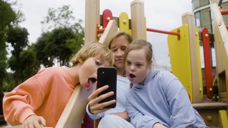 Close-up-view-of-a-little-girl-with-down-syndrome-and-her-friends-playing-with-smartphone-in-the-park-on-a-windy-day