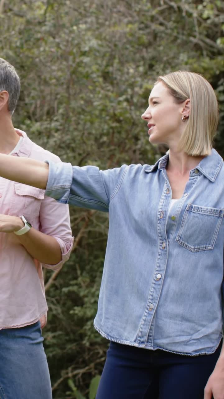 Video vertical: Mujer rubia hablando, vestida de mezclilla, levantando el brazo y señalando a la izquierda para mostrar el jardín, con reloj.