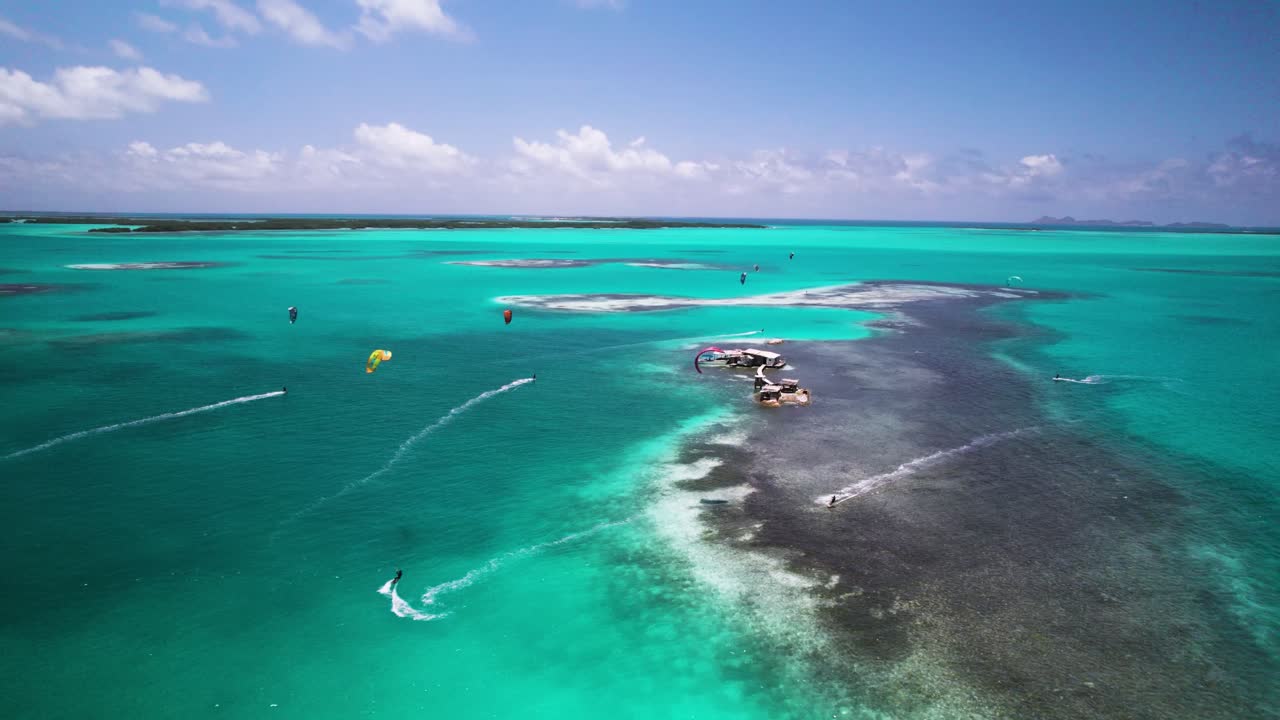 Kiteboarders riding turquoise waters near a remote island with palafitos, aerial view