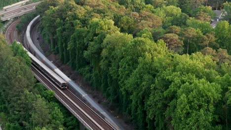 drone shot of atlanta metro rail and freight container shipping train crossing through nature forest trail, georgia state route 400, t harvey mathis parkway