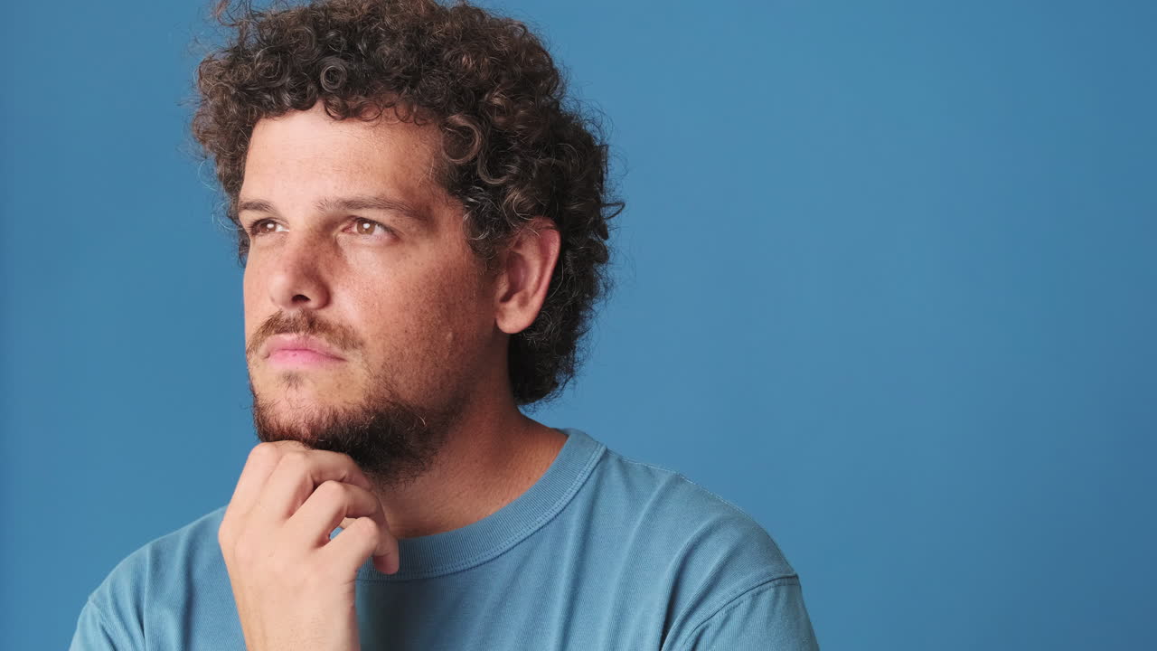 Thoughtful Man with Curly Hair Pondering on Blue Background