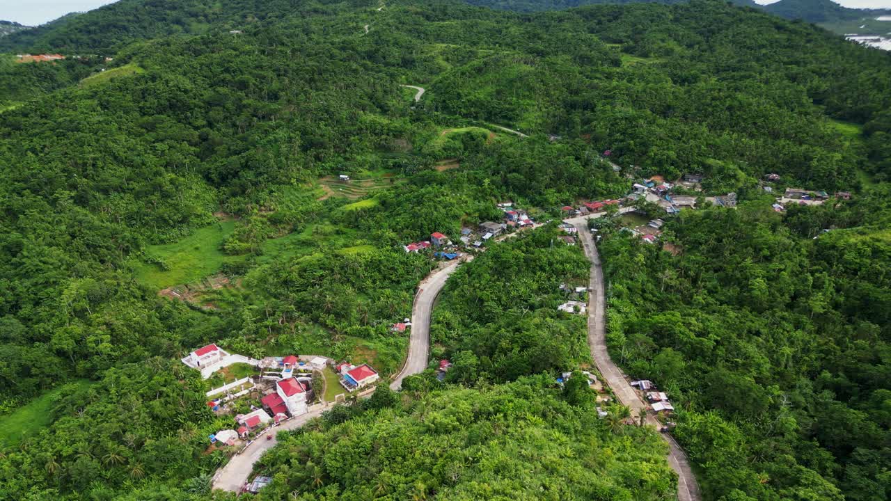 Overhead aerial drone shot of a tropical village barangay along lush mountains and winding roads at Bato, Catanduanes, Philippines