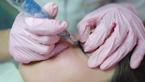 procedure of permanent makeup of eyes for women. the master is painting the client's eyes with a professional brush with a needle.