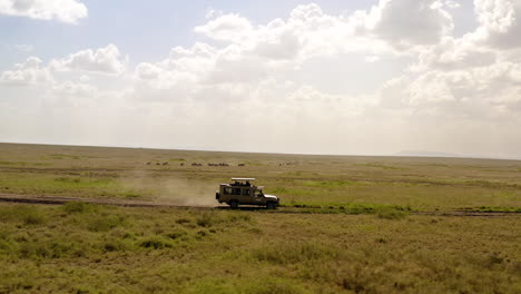 Safari-Tour-Coche-Conduciendo-Por-La-Carretera-A-Través-Del-Parque-Nacional-Serengeti-En-Un-Día-Soleado,-Con-Hermosas-Nubes-Grandes-Sobre-El-Horizonte,-Tanzania