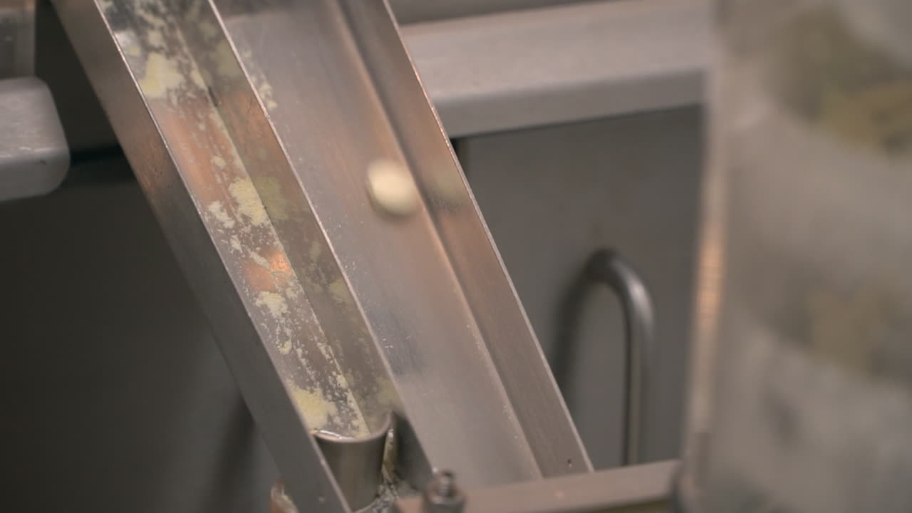 Small round pills fall down stainless steel ramp in pharma laboratory, still