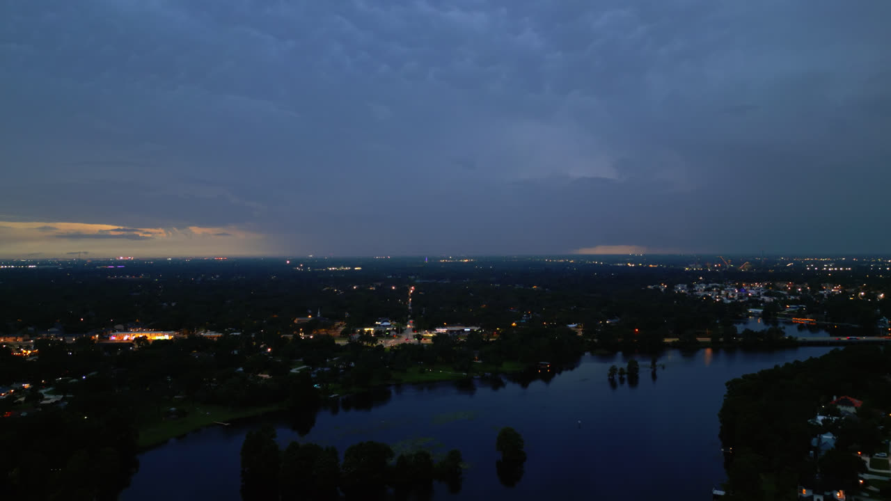 Twilight aerial over darkening water and city skyline, soft ambient light remains, dolly to street lights at dusk