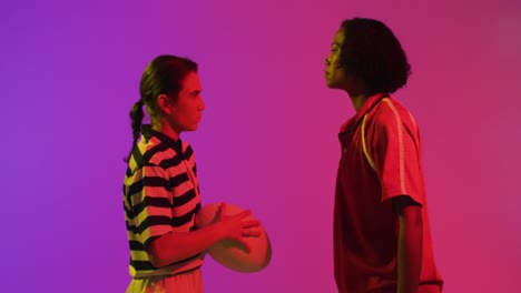 diverse female rugby players with rugby ball over neon pink lighting